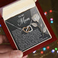 A person holds an open jewelry box featuring the Mom-Guiding Light - Interlocking Hearts Necklace in a rose gold finish, sparkling with cubic zirconia. A heartfelt "Mom" message on a rose-designed card is inside. The background softly twinkles with colorful lights.