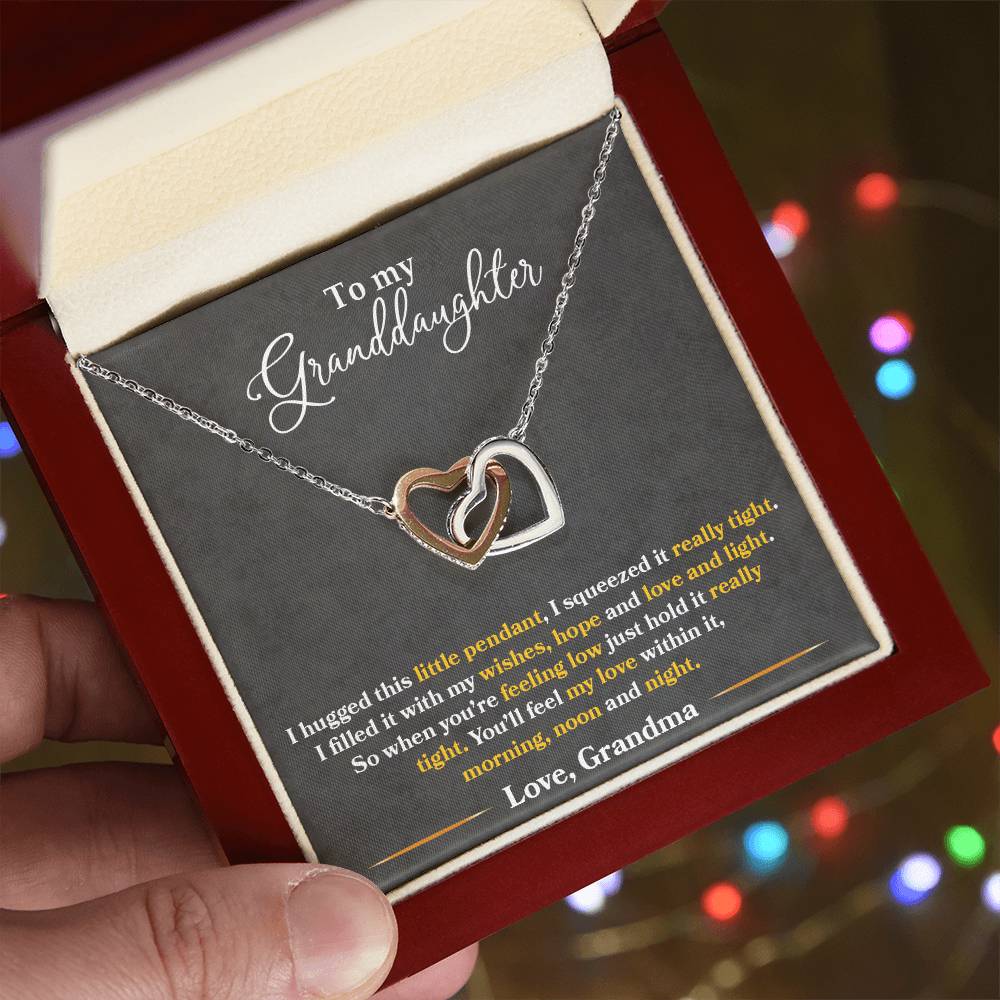 A person holding a gift box with a "To My Granddaughter, You'll Feel My Love Within This" - Interlocking Hearts Necklace from ShineOn Fulfillment, featuring cubic zirconia crystals and an emotional message from a grandmother to her granddaughter.