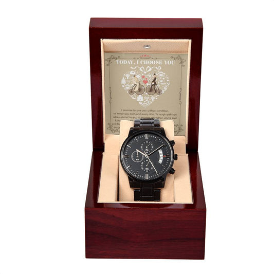 A black metal chronograph watch from the "To Husband, I Choose You" collection is elegantly displayed in an open wooden box. The box features an inscription reading "Today, I Choose You," complemented by additional text and illustrations in the background. The luxurious copper dial enhances the sophistication of this stunning timepiece.