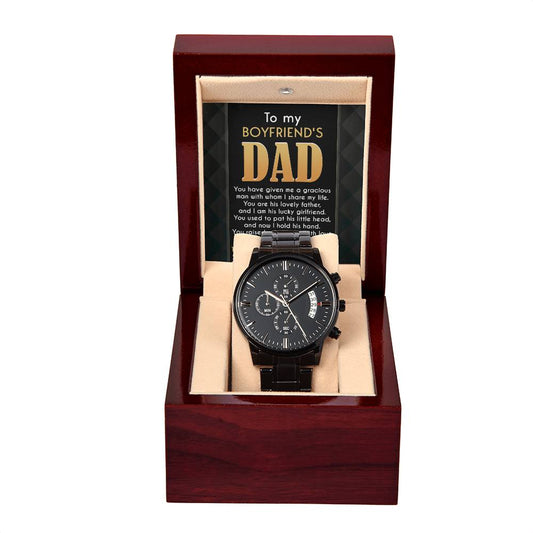 A black chronograph watch displayed in an open red wooden box with an affectionate message printed on the interior lid.