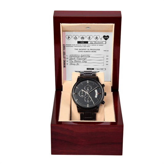 The "To Husband, Power of Love - Metal Chronograph Watch," featuring a black design with a dark face and calendar functions, is presented in an open wooden box engraved with a heartfelt message inside the lid.