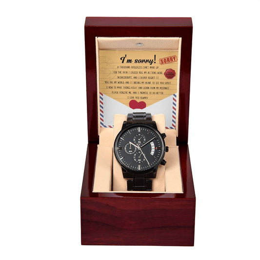 The "Sorry-Breaks My Heart - Metal Chronograph Watch," featuring a sleek black band, is elegantly displayed in an open wooden box. A note inside reads "I'm sorry!" followed by a brief apology message and a red heart illustration.