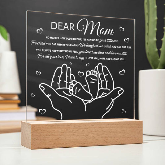 Sentence with Product Name: An "To Mom, Your Little One - Gift For Mom" acrylic plaque with a heartfelt message to a mother, featuring an illustration of two hands cradling smaller pair, displayed on a wooden stand.