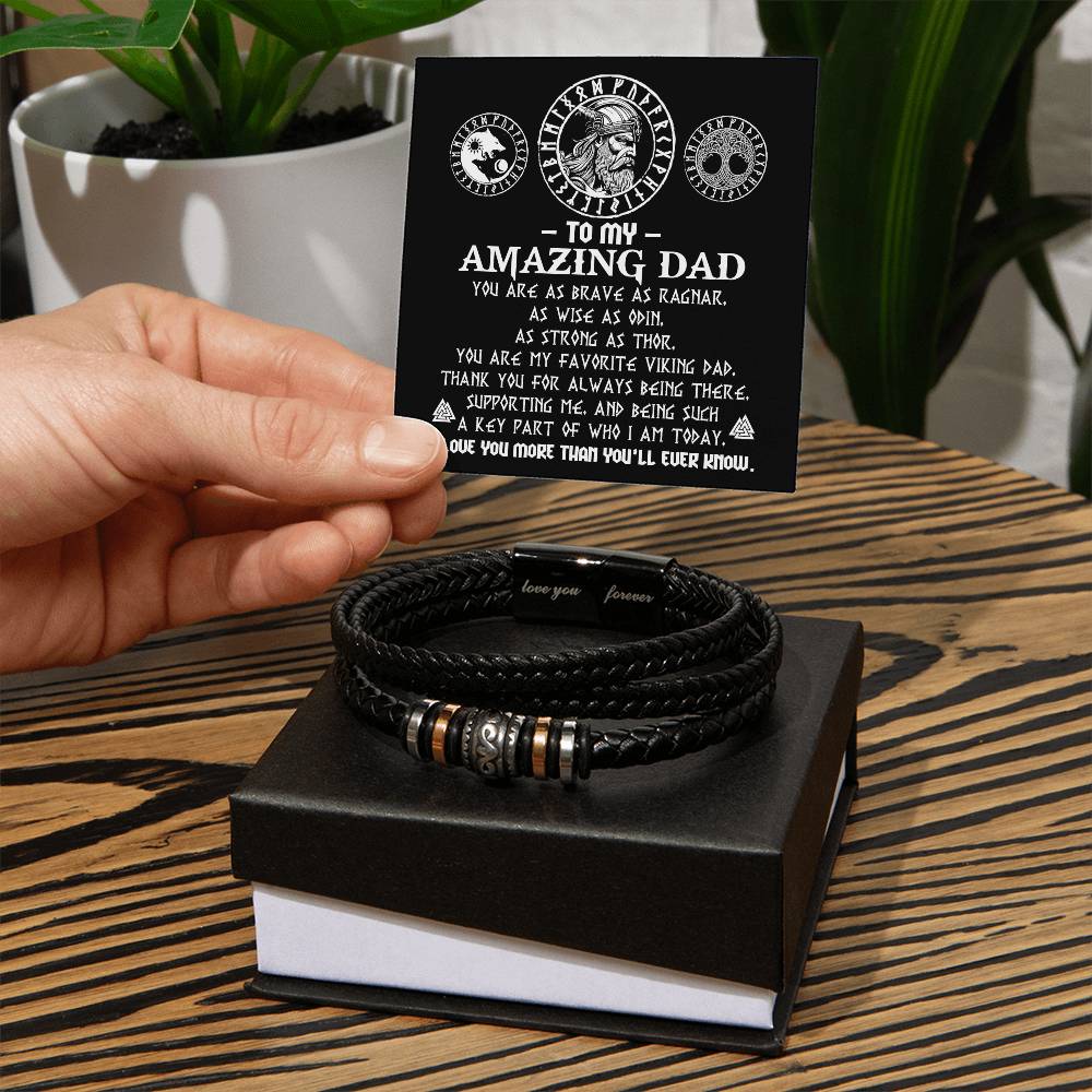 A hand holding a gift box containing a To Dad, Viking Dad - Love You Forever Bracelet and an open card addressed to "my amazing dad," praising him as a strong and supportive viking dad.