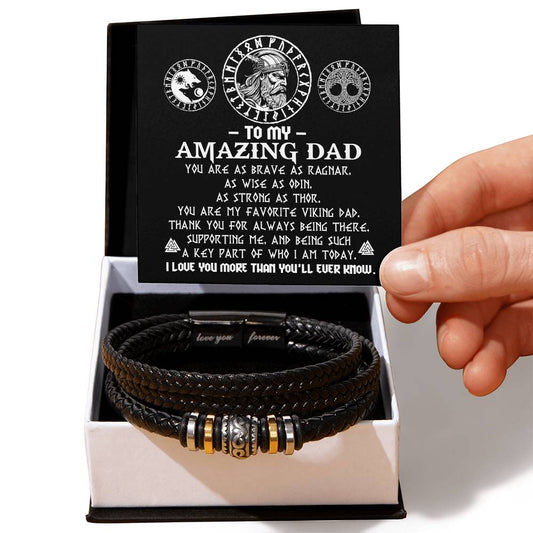 A hand holding a gift box containing a To Dad, Viking Dad - Love You Forever Bracelet and an open card addressed to "my amazing dad," praising him as a strong and supportive viking dad.
