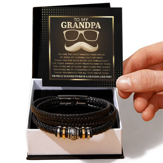 A hand presenting the "To Grandpa, Truly Blessed - Love You Forever" vegan leather bracelet in a gift box featuring a heartfelt message addressed to a grandpa.