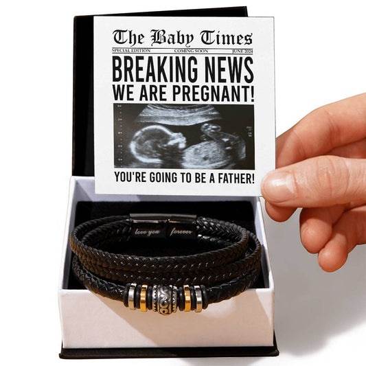 A hand holding a note designed like a newspaper announcing pregnancy above a box containing the To Father, The Baby Times - Love You Forever Bracelet—black braided with metallic accents, making the perfect gift for him to remember this special moment.