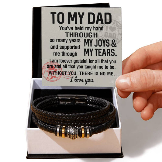 A hand holding a card with a heartfelt message to a dad. The card is next to the To Dad, Held My Hand - Love You Forever Bracelet, made of vegan leather, adorned with metal accents, and placed thoughtfully in a box.