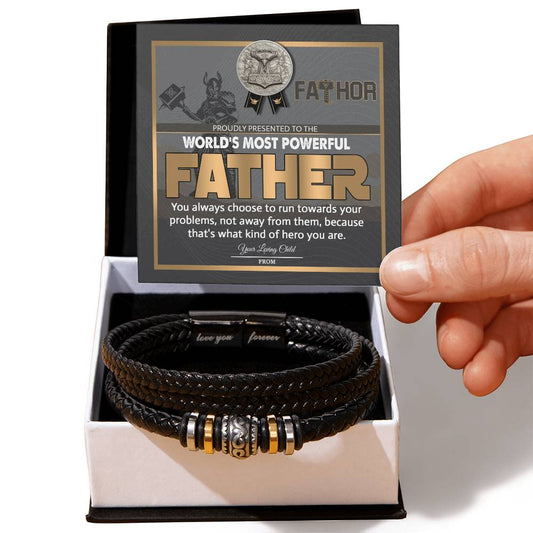 A hand holding a card that reads "World's Most Powerful Father" above a To Dad, Most Powerful Father - Love You Forever Bracelet with metallic accents in a gift box.