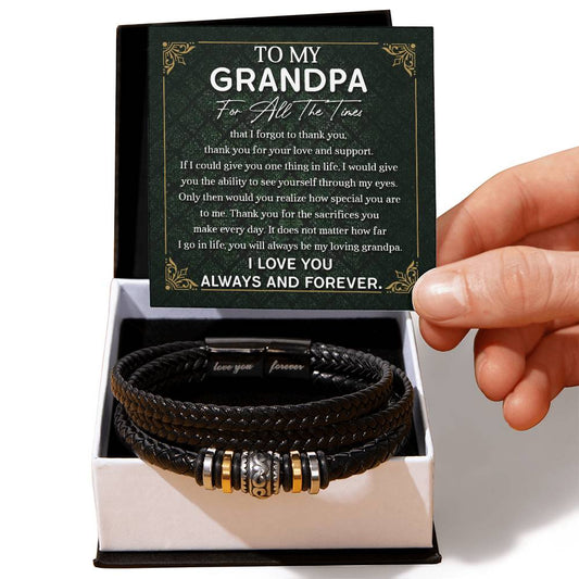 A hand holds a card that reads "To My Grandpa" above a decorative message. Below the card is a black vegan leather bracelet with metal accents in a white box—an ideal engraved gift for any special man, the "To Grandpa, Thank You - Love You Forever Bracelet.