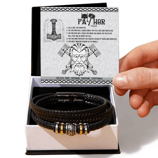 A hand holding a card titled "FATHOR" with an illustration and text, above a box containing a To Dad, Safe And Protected - Love You Forever Bracelet adorned with metallic decorations.