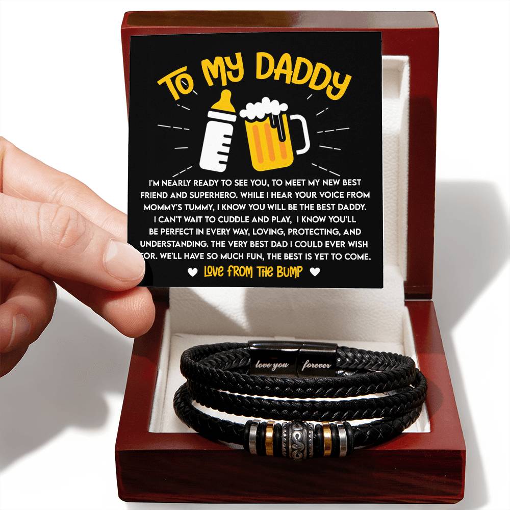 A hand holding a gift box containing a To Dad, To See You Love You Forever Bracelet and a card addressed "to my daddy" with a heartfelt message from an unborn child.