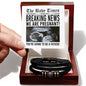 A hand holding a note designed like a newspaper announcing pregnancy above a box containing the To Father, The Baby Times - Love You Forever Bracelet—black braided with metallic accents, making the perfect gift for him to remember this special moment.