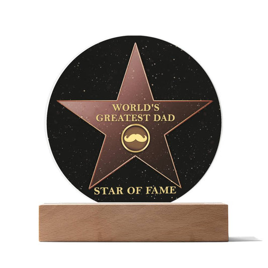 A premium acrylic plaque shaped like a Hollywood Walk of Fame star with a mustache icon that reads "To Dad, Greatest Dad - Acrylic Circle Plaque" and "Star of Fame." The plaque, ideal as a gift for special occasions, stands on a wooden base.