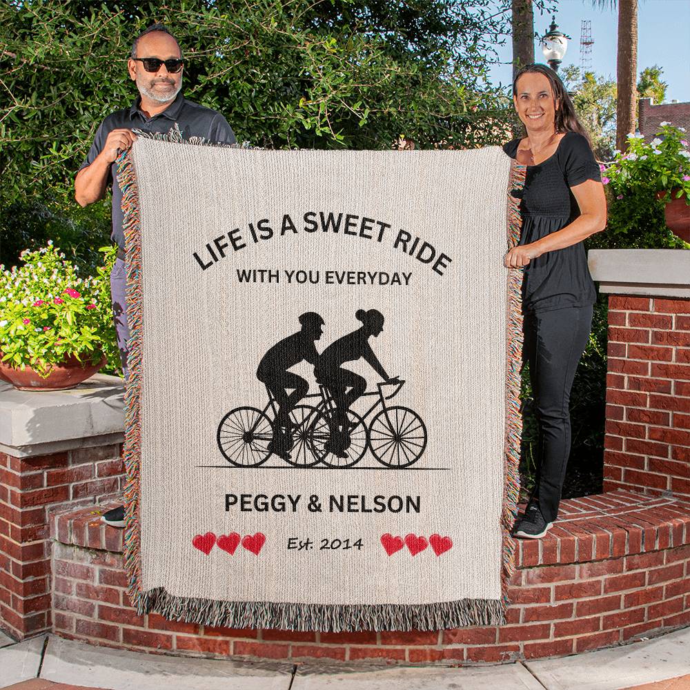 A couple holding a Personalized Life Is A Sweet Ride Cycling Couple Heirloom Woven Blanket, created by ShineOn Fulfillment. This blanket offers a cozy touch to your home decor, displaying as a beautiful wall hanging with its personalized design and high craftsmanship.