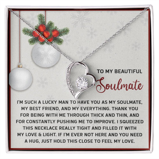 The Soulmate-Feel My Love - Forever Love Necklace, featuring a heart-shaped design adorned with CZ crystal, is presented elegantly on a card with a gold finish. It is enhanced by holiday-themed decorations with ornaments and greenery, and it includes a heartfelt message for your soulmate.