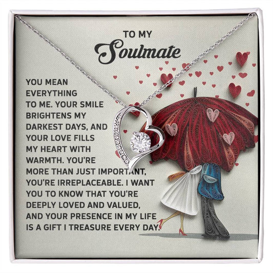 The Soulmate-Deeply Loved - Forever Love Necklace shines with a heart-shaped pendant in a gold finish, displayed on a card depicting a couple under a heart-patterned umbrella, adorned with CZ crystal details. It includes an enchanting love message.