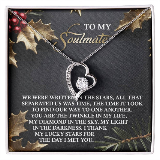 The Soulmate-In The Stars - Forever Love Necklace showcases a heart-shaped design with a solitaire gem set in cubic zirconia, presented on a dark gift box adorned with holly decorations and a romantic message. A subtle gold finish adds an extra touch of elegance to this timeless piece.