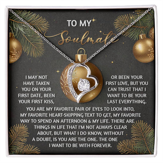 The Soulmate-Without A Doubt - Forever Love Necklace showcases a heart-shaped pendant with a gold finish, beautifully presented on a card featuring a romantic message. Sparkling CZ crystals enhance its allure, while pine branches provide a charming background.