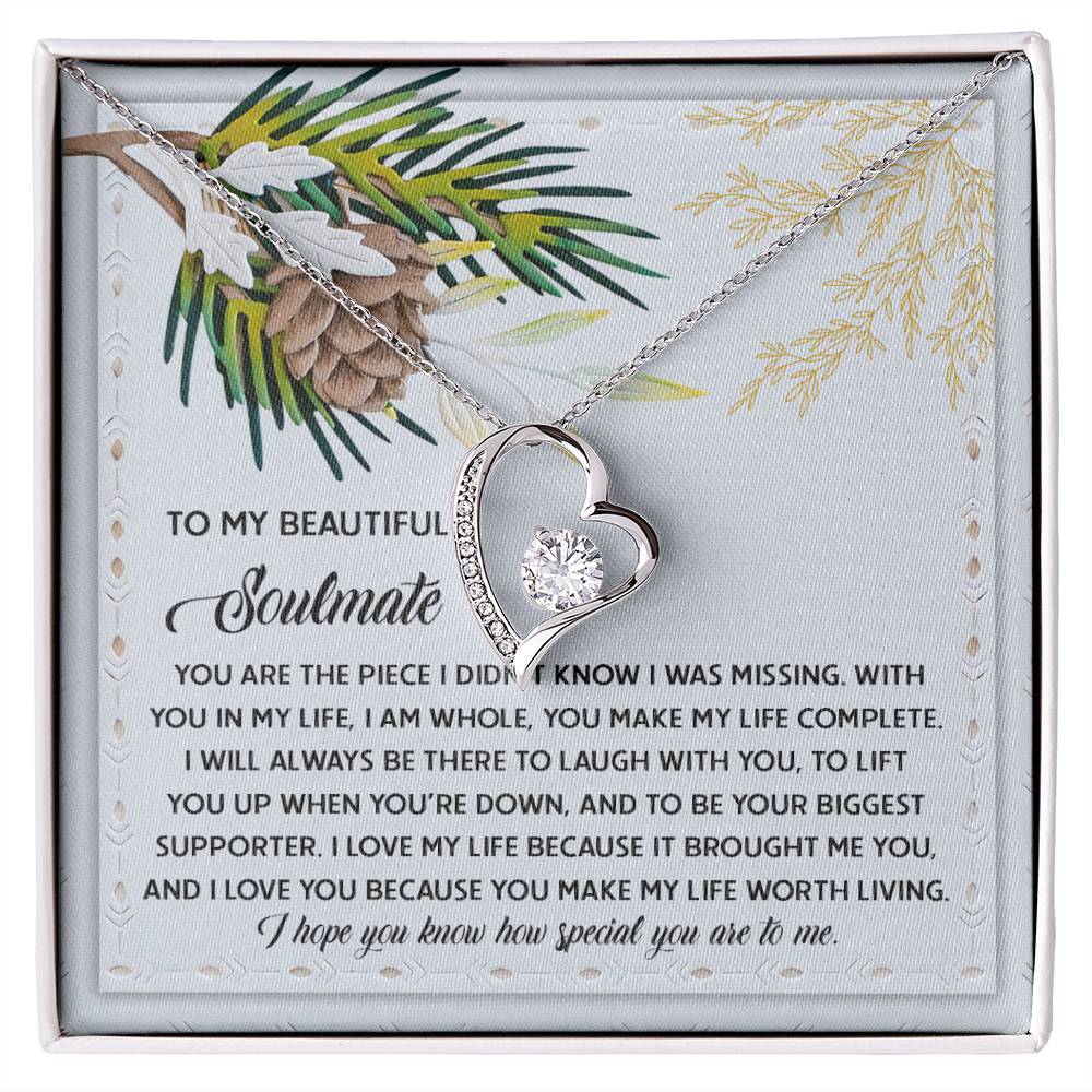 The Soulmate-Biggest Supporter - Forever Love Necklace, featuring a heart-shaped pendant adorned with cubic zirconia, rests elegantly in its box decorated with romantic text and a charming pinecone design.