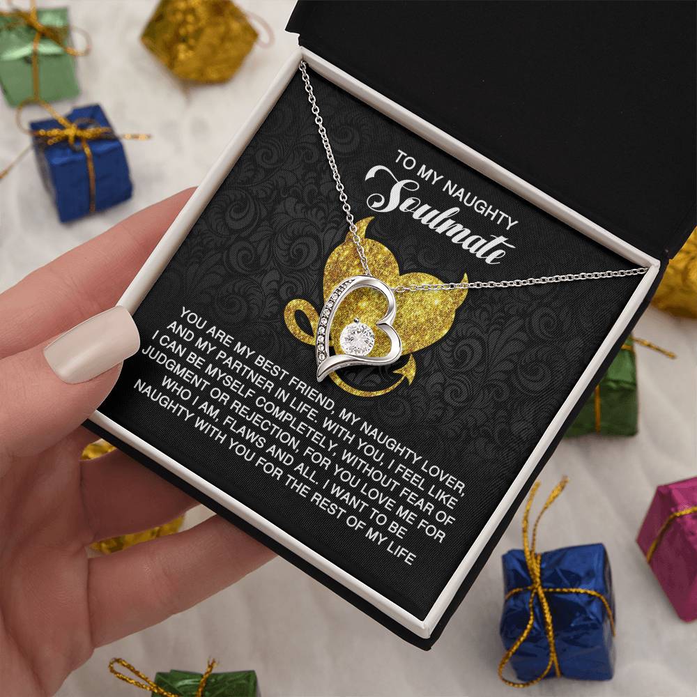 A hand reveals the "Soulmate-Naughty With You - Forever Love Necklace" inside a jewelry box. The heart-shaped necklace, with a cubic zirconia stone, is accompanied by a card that reads "To My Naughty Soulmate." It shines with its gold finish amid colorful gift boxes.