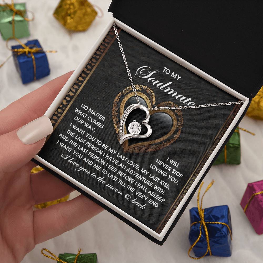 A hand presents the Soulmate-The Very End - Forever Love Necklace in a box. Inside, a card has a soulmate message. The necklace, adorned with cubic zirconia and 14k white gold finish, is surrounded by colorful gift boxes.