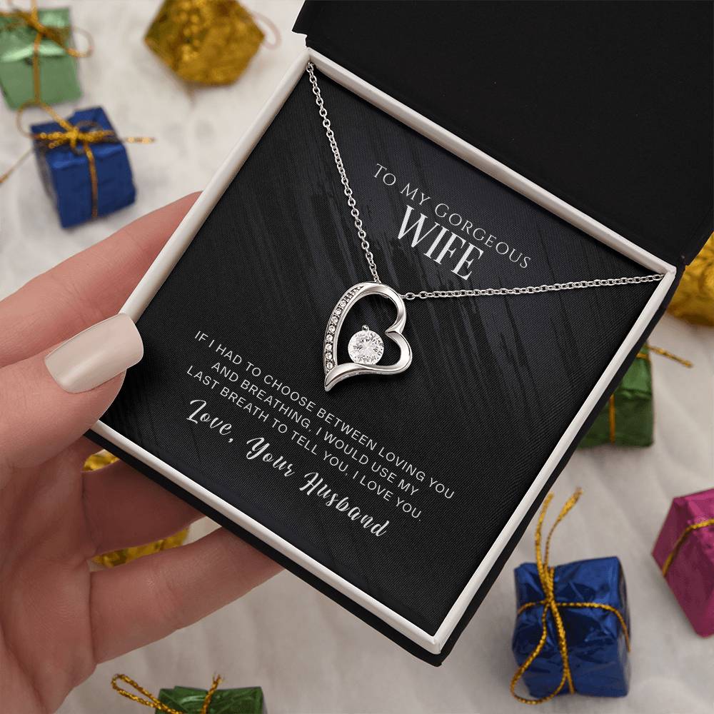 A hand holding an open jewelry box with a ShineOn Fulfillment To My Wife, I Love You - Forever Love Necklace featuring a heart-shaped pendant adorned with CZ crystal and a loving message from a husband to a wife, all elegantly finished in gold.