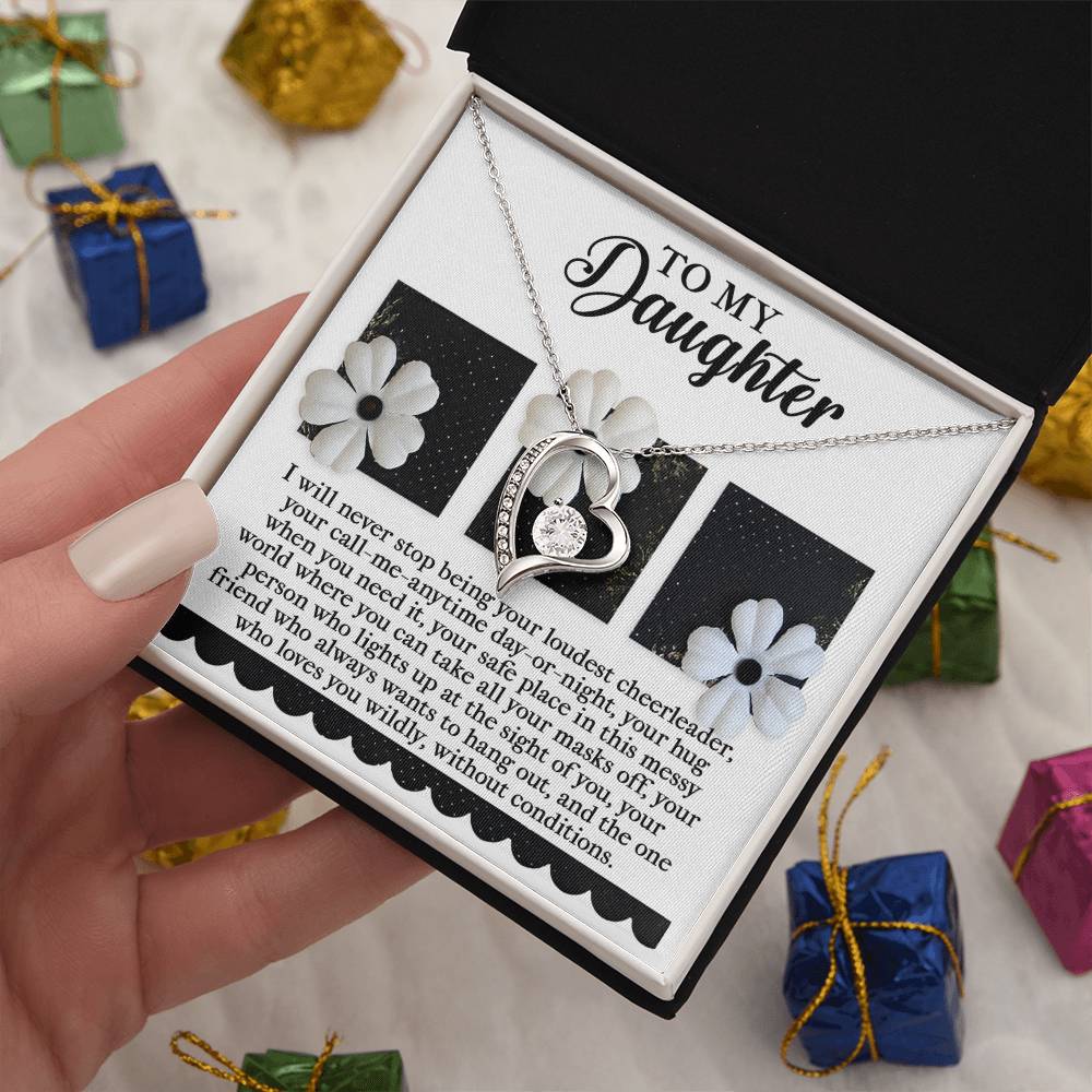 The Daughter-Loudest Cheerleader - Forever Love Necklace, featuring a heart pendant, glimmers in an open box with the message "To My Daughter." Adorned with a gold finish and shimmering CZ crystal, it rests amid decorative flowers and text. Small gift boxes peek from the background, completing the heartfelt scene.