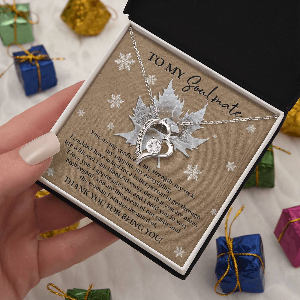 A hand presents a box containing the Soulmate-Our Castle - Forever Love Necklace, embellished with a CZ crystal and a gold finish. The card reads "To My Soulmate." In the background, small gifts wrapped in colorful paper await.