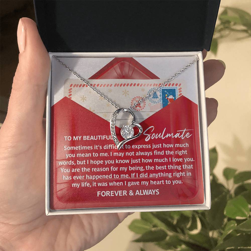 A hand presents an open gift box displaying the "Soulmate-Right Words - Forever Love Necklace," featuring a heart-shaped pendant adorned with a sparkling CZ crystal and a white gold finish. Accompanying the necklace is a card containing a heartfelt message, perfectly enhancing this elegant symbol of love.