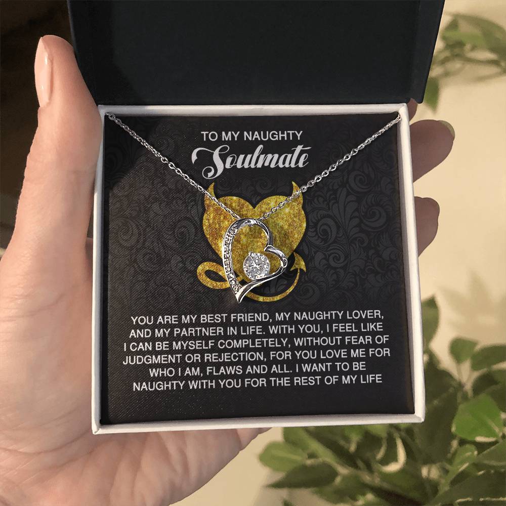 A hand holds the Soulmate-Naughty With You - Forever Love Necklace in a gift box. The interconnected hearts have a gold finish and cubic zirconia stones. The box lid reads "To My Naughty Soulmate" with a heartfelt message below.