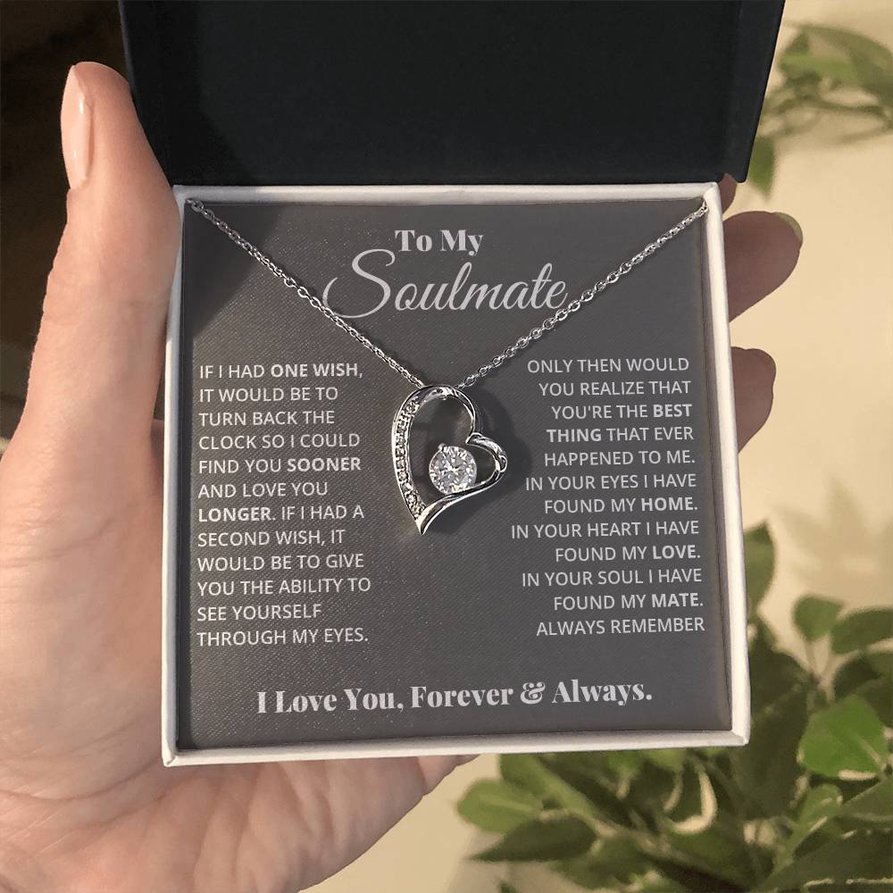 A hand holding an open jewelry box with a heart-shaped Cubic Zirconia ShineOn Fulfillment Forever Love Necklace and a sentimental message for a soulmate, all sparkling with a gold finish.