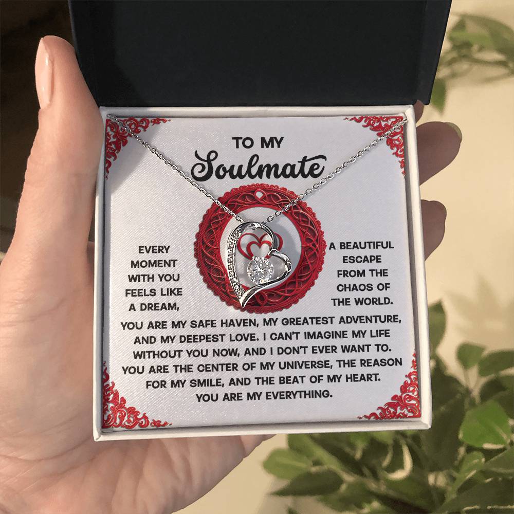 A hand displays an open box containing the Soulmate-Like A Dream - Forever Love Necklace, featuring a cubic zirconia stone set in white gold finish. A heartfelt message for a soulmate, surrounded by red designs and love-filled text, accompanies this exquisite piece.