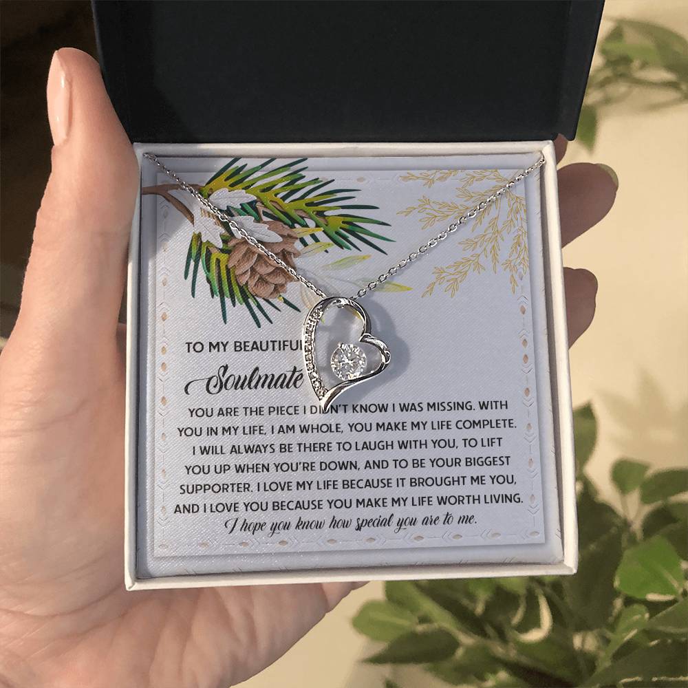 A hand holding an open jewelry box reveals the Soulmate-Biggest Supporter - Forever Love Necklace, which features a heart-shaped pendant adorned with sparkling CZ crystal, elegantly set against a card with a sentimental message.