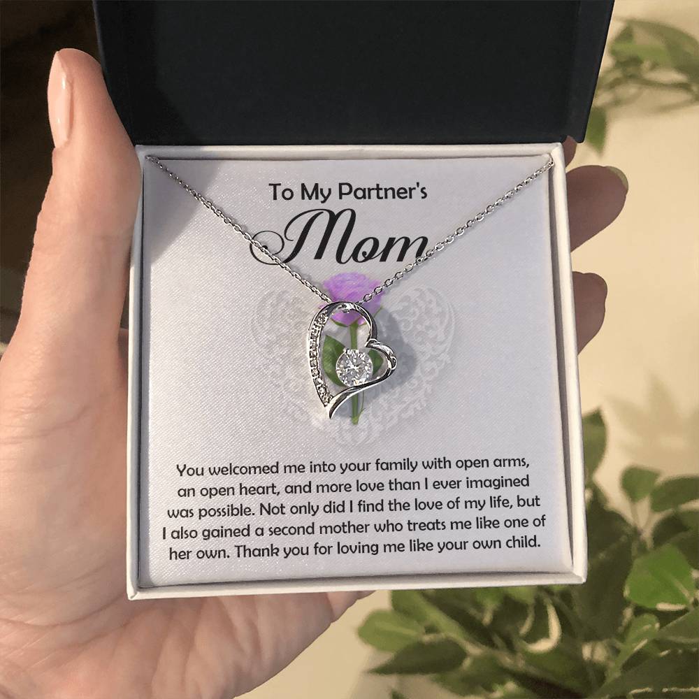 A hand holds an open jewelry box with the "Partner's Mom-A Second Mother - Forever Love Necklace," featuring a white gold finish and CZ crystal, beside a heartfelt message: "To My Partner's Mom," expressing gratitude and love.