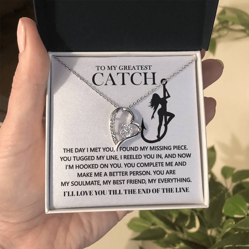 A hand holds an open box with the Soulmate-Hooked On You - Forever Love Necklace, featuring a heart-shaped pendant and cubic zirconia stone. Beside a message on love and companionship is a silhouette of someone fishing, beautifully complemented by the necklace's white gold finish.