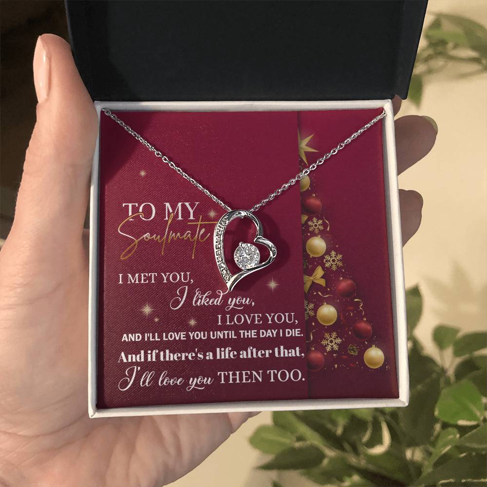 A hand presents a Soulmate-Love You Then - Forever Love Necklace in an open box with a romantic message and Christmas tree design on a red background. The heart-shaped pendant sparkles with cubic zirconia, ideal for honoring your soulmate this holiday season.