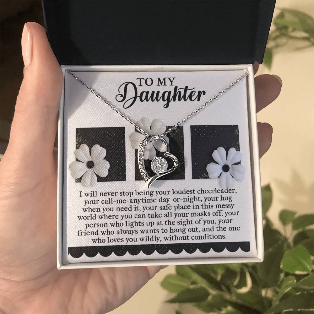 A hand presents an open box displaying the Daughter-Loudest Cheerleader - Forever Love Necklace. The inside of the box lid features a touching message titled "To My Daughter" alongside floral imagery. The heart-shaped necklace, embellished with sparkling CZ crystals and a radiant gold finish, embodies eternal love.