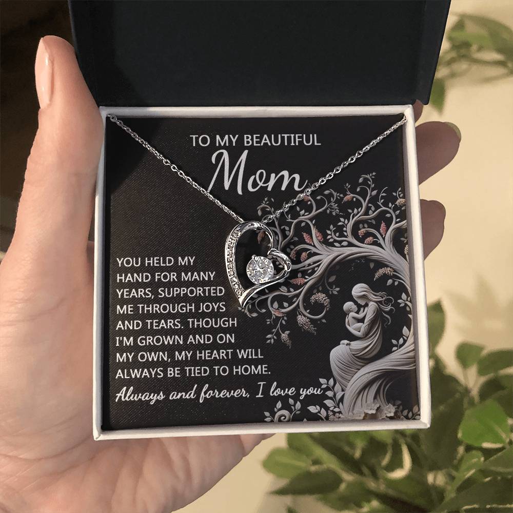 A hand holds an open box containing a heart-shaped "To Mom, On My Own - Forever Love Necklace" with a pendant and the text: "To My Beautiful Mum, You Held My Hand For Many Years...Always and forever, I love you." This personalized gift will be cherished for its elegance and sentiment.