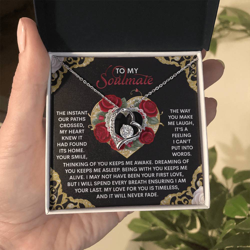 A hand holds a box containing the Soulmate-Never Fade - Forever Love Necklace, with a heart-shaped pendant featuring a rose design and sparkling CZ crystals. Available in white gold or yellow gold finish, the box includes a romantic message to a soulmate.