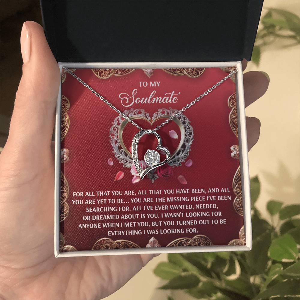 A hand opens a gift box revealing the Soulmate-I Met You - Forever Love Necklace with a heart-shaped pendant and white gold finish. The 6.5mm CZ crystal sparkles, and the box's red interior displays a soulmate message surrounded by decorative hearts.