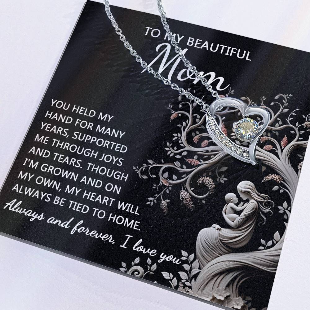 The "To Mom, On My Own - Forever Love Necklace" is a beautiful silver heart-shaped necklace presented on a card with the heartfelt message, "To My Beautiful Mom: You held my hand for many years, supported me through joys and tears. Though I'm grown and on my own, my heart will always be tied to home." This personalized gift is completed with a sparkling cubic zirconia stone.