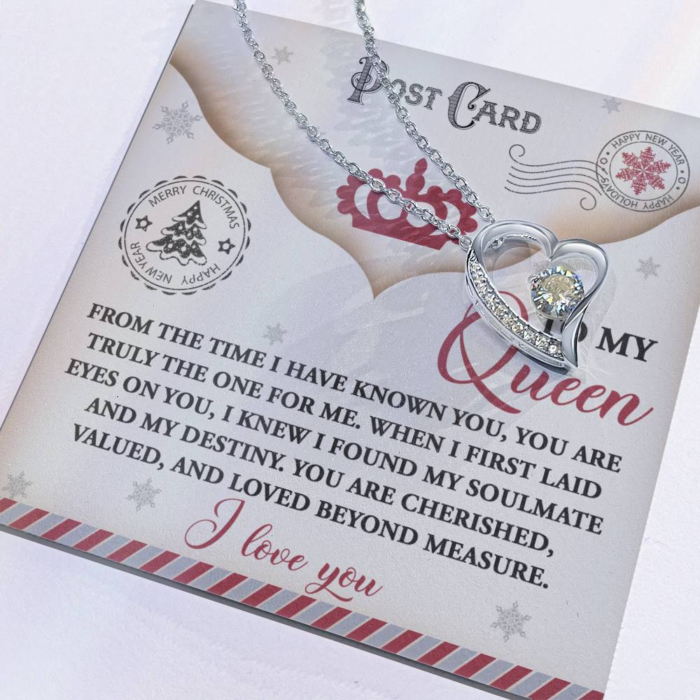 The Soulmate-The One - Forever Love Necklace, featuring a gold finish and a heart-shaped pendant adorned with shimmering cubic zirconia stones, elegantly sits on a greeting card with a romantic message addressed to "My Queen" for Christmas.