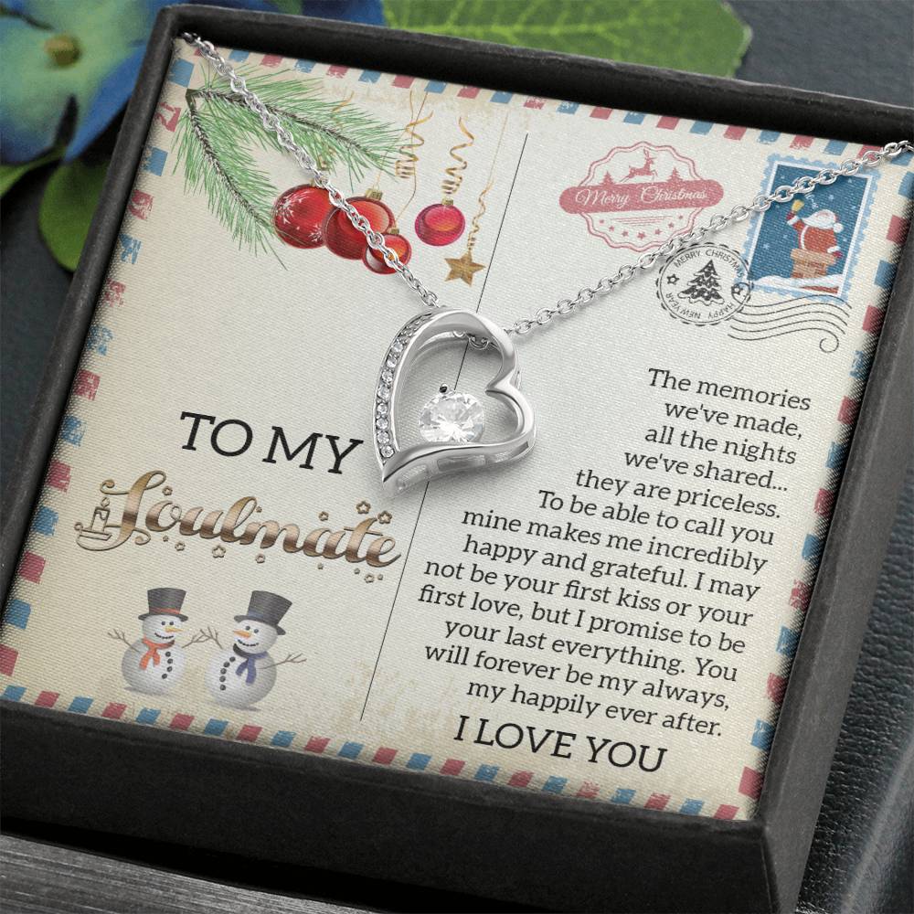 The Soulmate-Last Everything - Forever Love Necklace, featuring a central gem and CZ crystal, hangs gracefully with its white gold finish. It is presented on a card with a heartfelt message and is encircled by holiday decorations such as snowmen and ornaments.