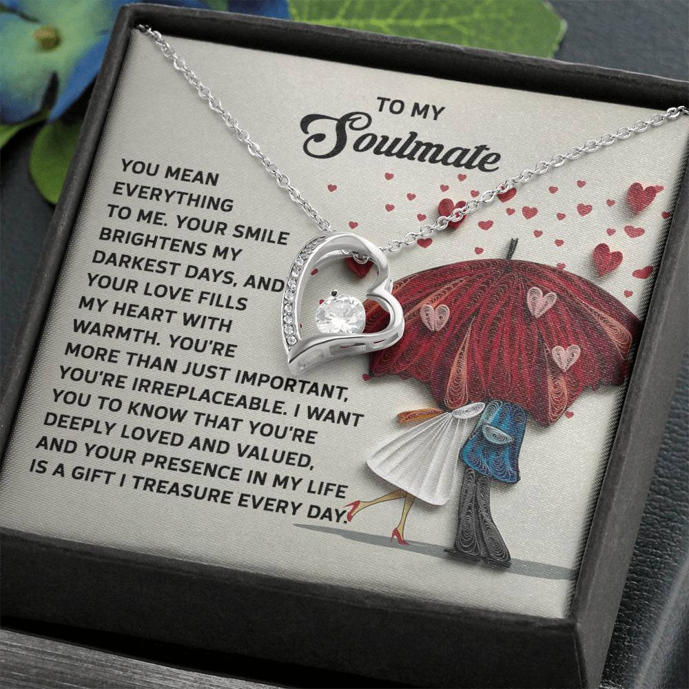 The Soulmate-Deeply Loved - Forever Love Necklace features a heart-shaped charm in white gold finish, adorned with a dazzling CZ crystal. It comes in a box with a romantic message and depicts a couple under a heart-decorated umbrella, symbolizing eternal affection.