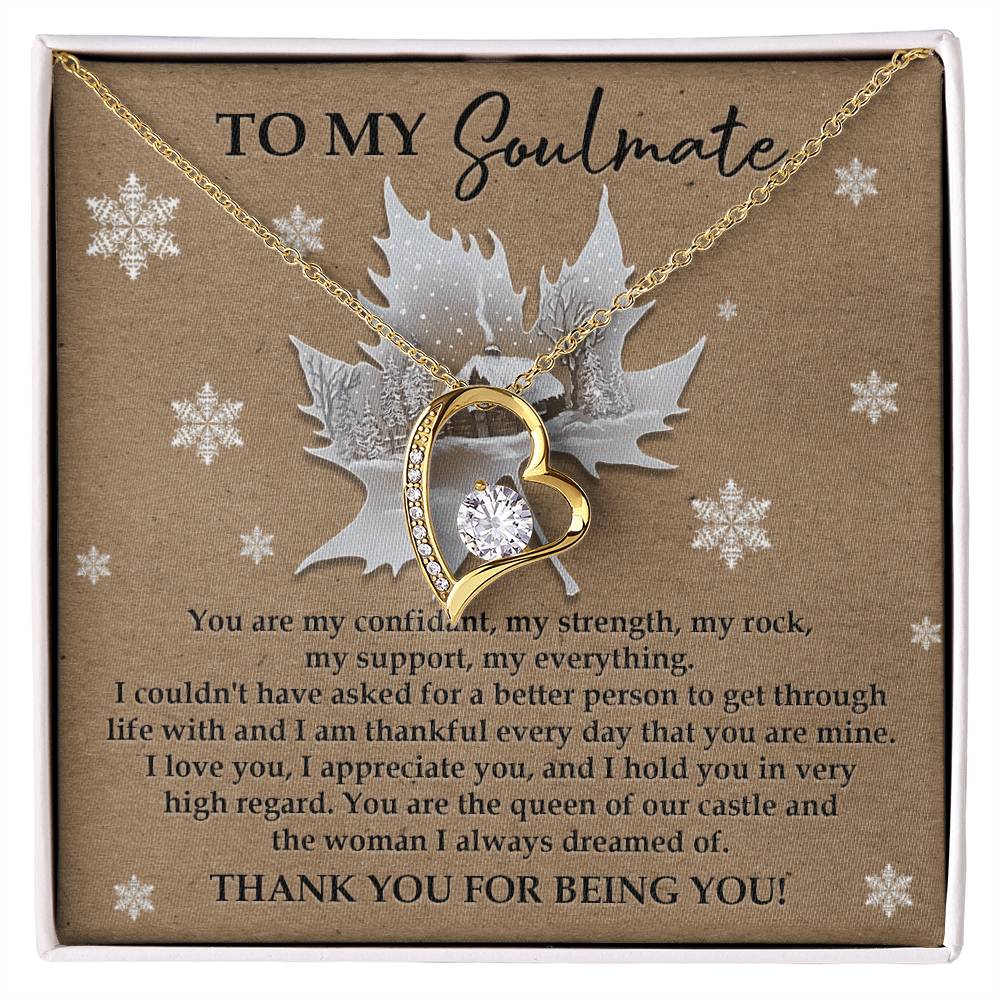 A necklace with a gold-finish and heart-shaped design, featuring a central cubic zirconia stone, is showcased in a box. The background includes a romantic message meant for a soulmate along with snowflake decorations, embodying the essence of the Soulmate-Our Castle - Forever Love Necklace.