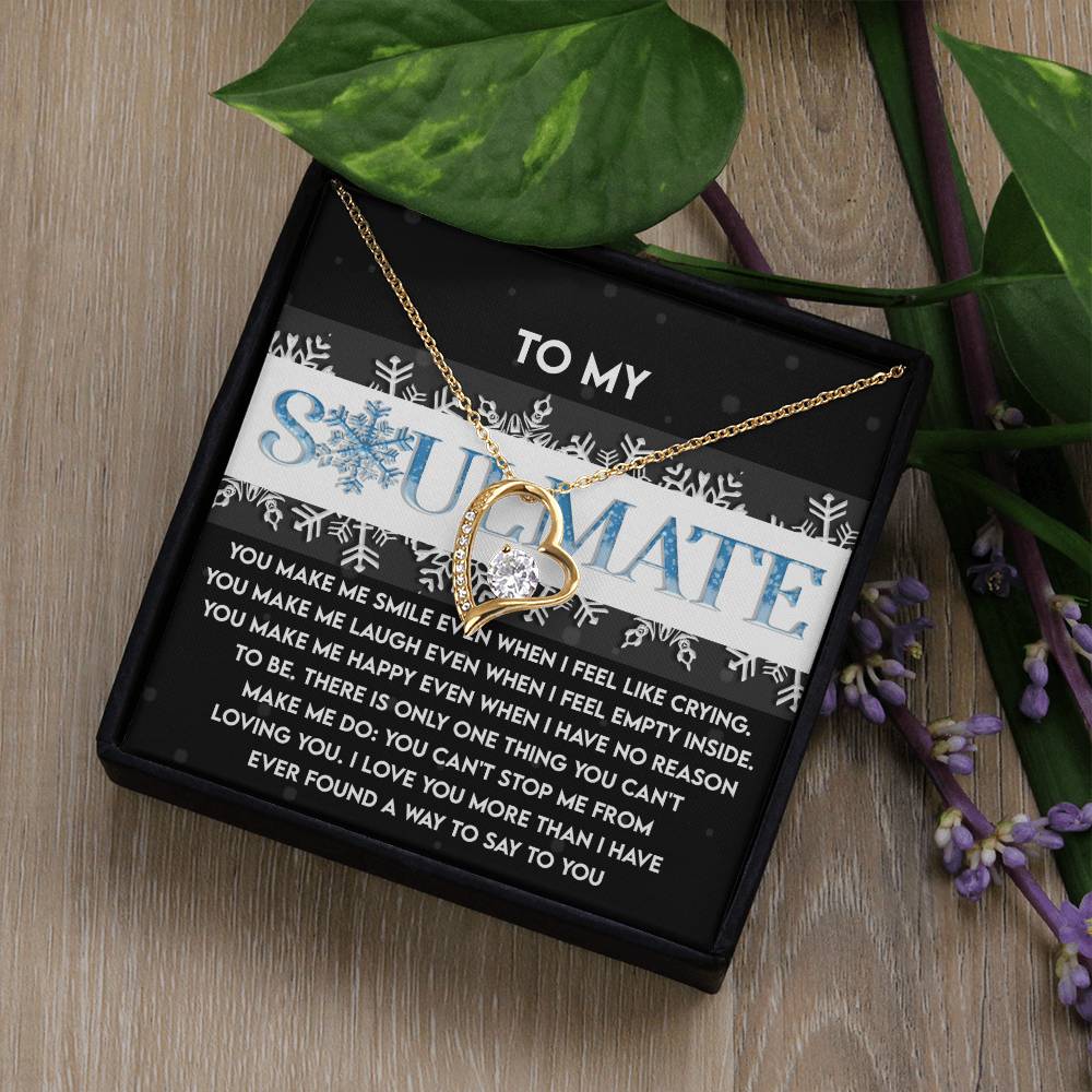 A Soulmate-Loving You - Forever Love Necklace featuring a cubic zirconia pendant is showcased on a card that reads "To My Soulmate." Nestled in a gift box with a heartfelt message, it rests gracefully on a wooden surface adorned with green leaves and purple flowers, all complemented by its exquisite gold finish.