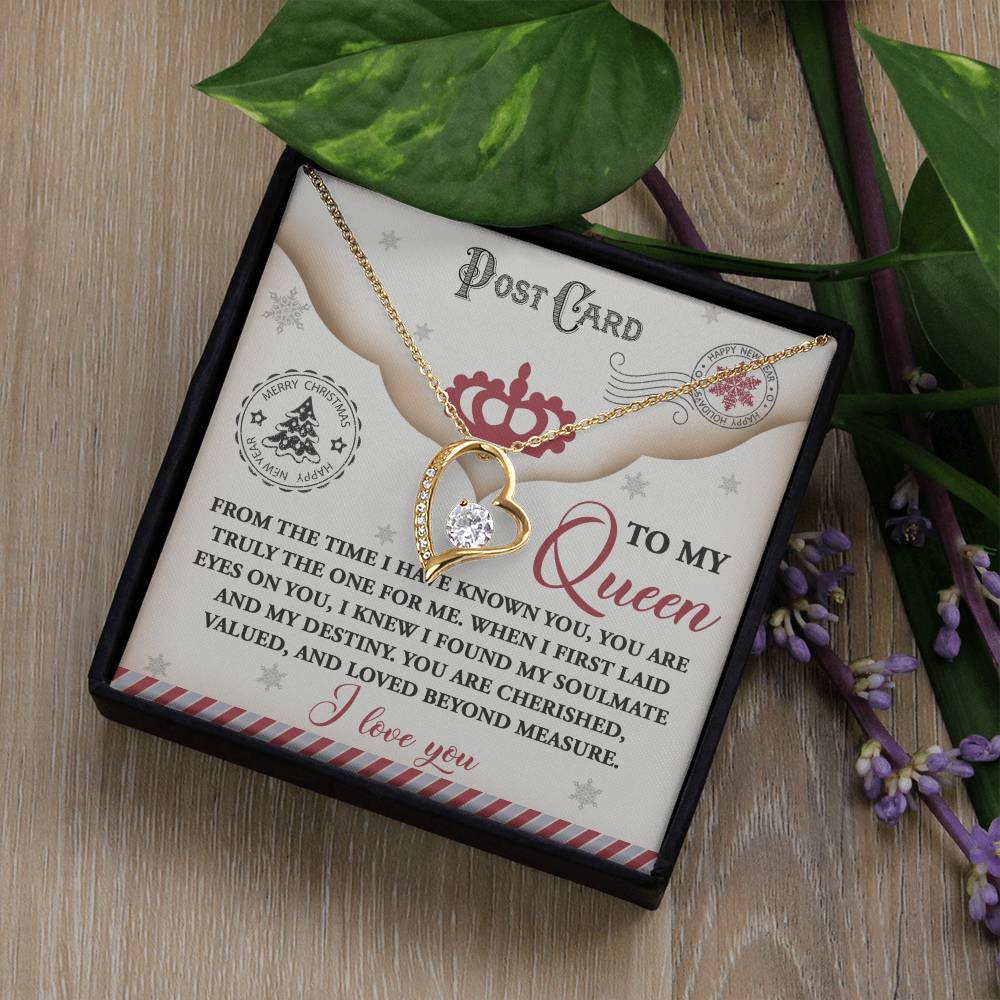 The Soulmate-The One - Forever Love Necklace features a gold finish with a heart pendant and comes beautifully presented on a "To My Queen" postcard inside an elegant box, surrounded by green leaves and purple flowers. Adorned with sparkling cubic zirconia, it is the perfect gift for someone special.