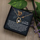 The Soulmate-Eternal Happiness - Forever Love Necklace, a gold heart-shaped piece with a dazzling CZ crystal, rests in an open jewelry box. Its lid features an embossed floral design and a heartfelt love and happiness message, elegantly set against a wood surface with scattered leaves and flowers.