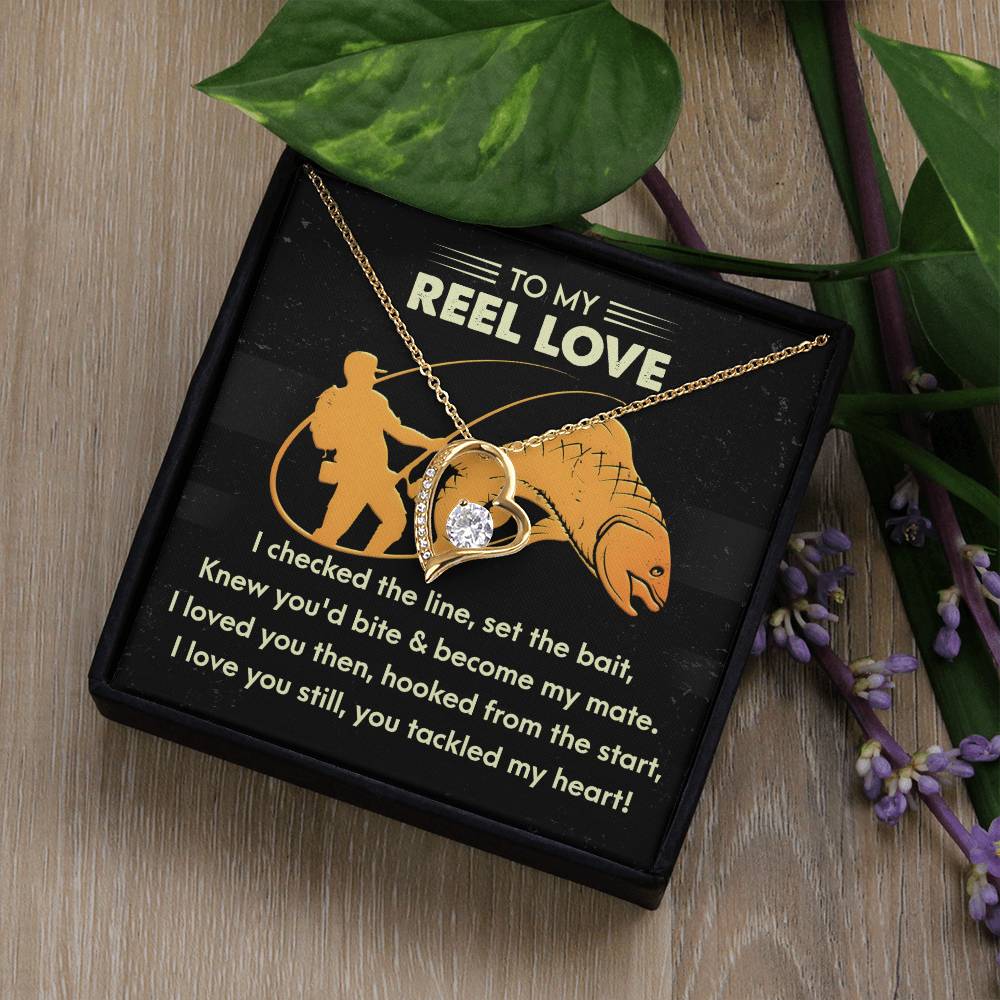 Displayed on a black card with "To My Reel Love," this Forever Love Necklace features a fish and hook design, CZ crystals, and a gold finish. The box is adorned with green leaves and purple flowers. Product Name: Soulmate-Tackled My Heart - Forever Love Necklace.